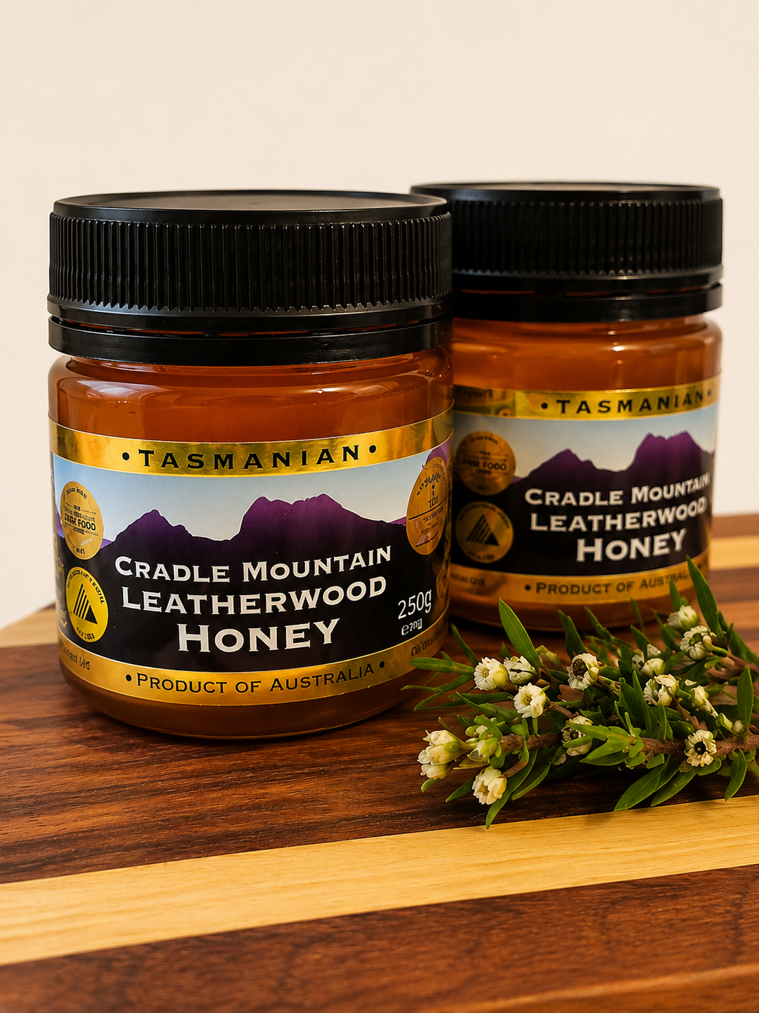 Cradle Mountain Leatherwood Honey on a wooden serving board with Leatherwood blossom, showcasing premium 100% Tasmanian honey.